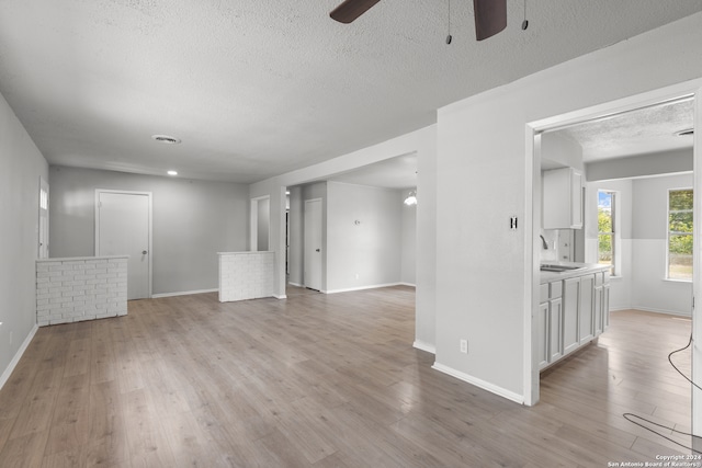 unfurnished living room with a textured ceiling, light hardwood / wood-style floors, ceiling fan, and sink