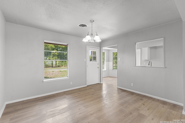 unfurnished room featuring an inviting chandelier, light hardwood / wood-style floors, and a textured ceiling