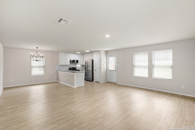 unfurnished living room with light hardwood / wood-style flooring, a notable chandelier, and a healthy amount of sunlight