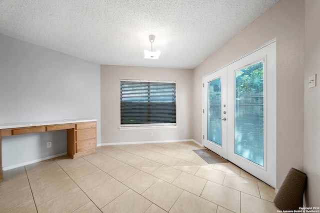 interior space with a textured ceiling, light tile patterned flooring, and french doors