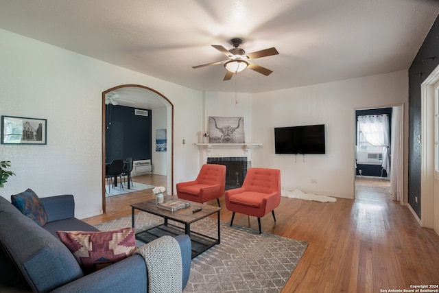 living room featuring light wood-type flooring, a tile fireplace, and ceiling fan