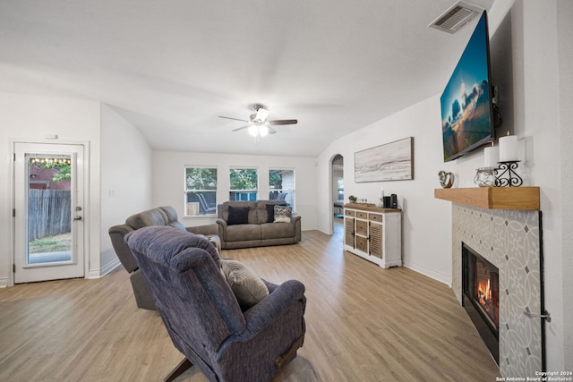 living room with light wood-type flooring, vaulted ceiling, ceiling fan, and a stone fireplace