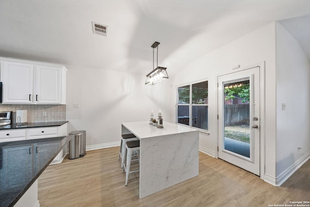 kitchen with a center island, white cabinets, hanging light fixtures, light hardwood / wood-style flooring, and decorative backsplash