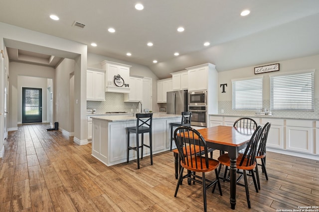 dining room with sink, light wood-type flooring, and vaulted ceiling