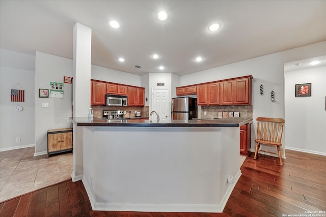 kitchen featuring backsplash, kitchen peninsula, dark hardwood / wood-style floors, and stainless steel appliances