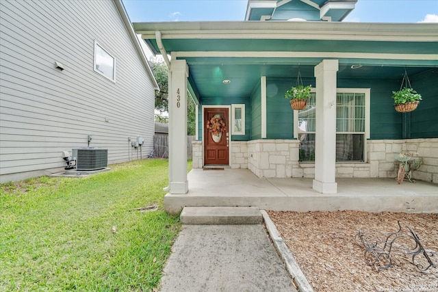 view of exterior entry with a lawn, a porch, and central AC