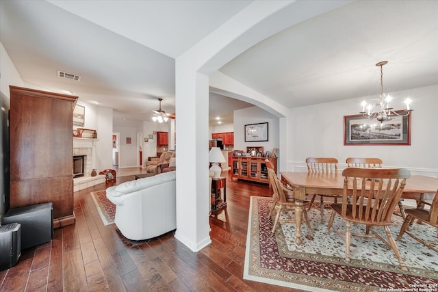 dining space with ceiling fan with notable chandelier, a tile fireplace, and dark hardwood / wood-style flooring