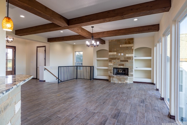 unfurnished living room featuring built in features, beam ceiling, an inviting chandelier, a fireplace, and dark hardwood / wood-style flooring