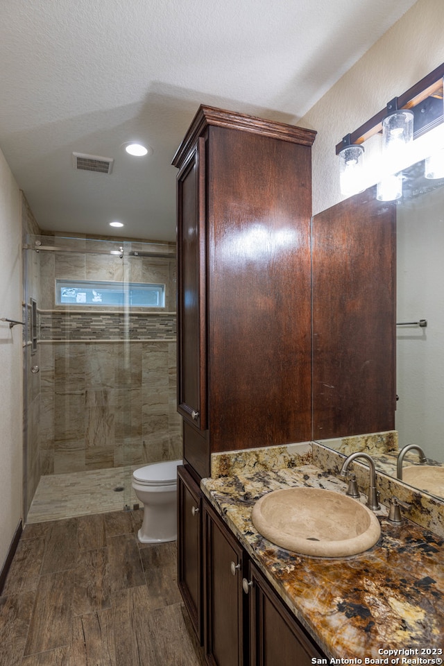 bathroom featuring vanity, walk in shower, a textured ceiling, hardwood / wood-style flooring, and toilet