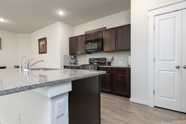 kitchen featuring light stone counters, stainless steel gas range oven, backsplash, and light hardwood / wood-style floors