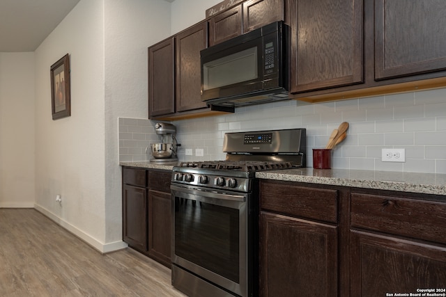 kitchen with dark brown cabinets, gas stove, light hardwood / wood-style floors, decorative backsplash, and light stone countertops