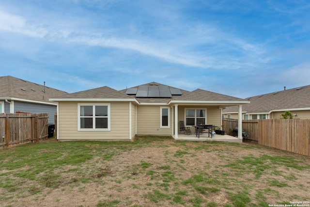 back of property with a patio, a yard, and solar panels