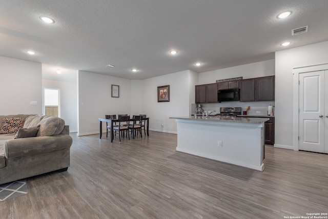 kitchen with dark brown cabinets, light hardwood / wood-style floors, a textured ceiling, stainless steel stove, and a center island with sink