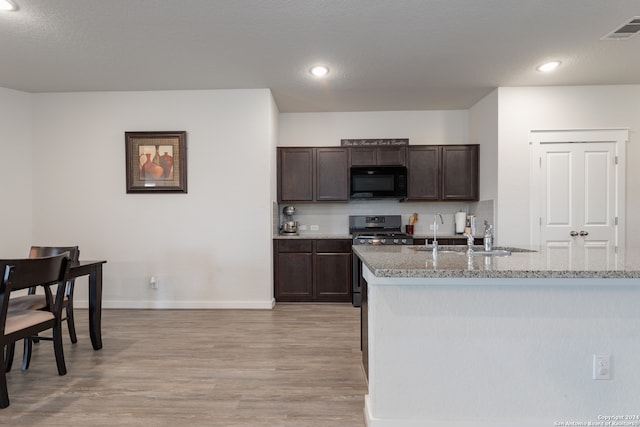 kitchen featuring dark brown cabinetry, sink, light hardwood / wood-style flooring, stainless steel stove, and light stone countertops