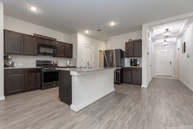 kitchen with dark brown cabinetry, a center island with sink, stainless steel appliances, and light hardwood / wood-style flooring