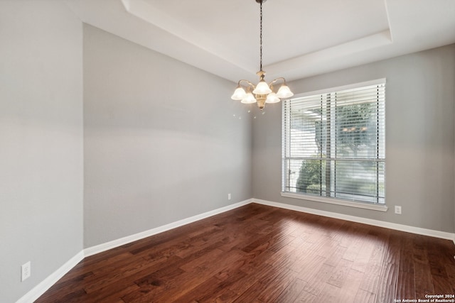 empty room featuring hardwood / wood-style flooring, a tray ceiling, and a chandelier