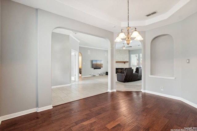 spare room with light hardwood / wood-style flooring, a chandelier, and a stone fireplace