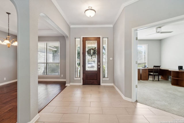 entrance foyer with ceiling fan with notable chandelier, a wealth of natural light, ornamental molding, and light carpet