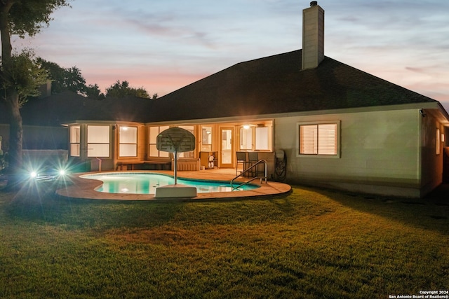 back house at dusk featuring a yard and a patio