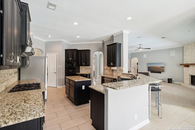 kitchen featuring sink, kitchen peninsula, black appliances, a stone fireplace, and ceiling fan