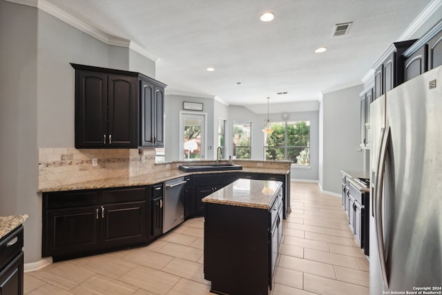 kitchen featuring appliances with stainless steel finishes, hanging light fixtures, light stone counters, a center island, and sink