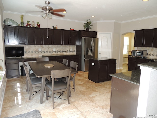 kitchen with ceiling fan, ornamental molding, a kitchen island, stainless steel refrigerator with ice dispenser, and dark stone countertops