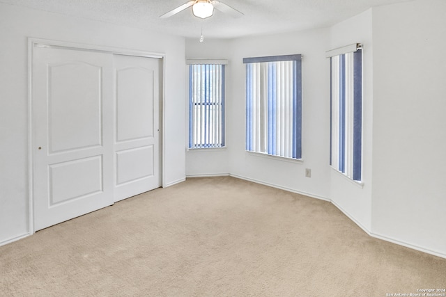 unfurnished bedroom featuring light carpet, a closet, ceiling fan, and a textured ceiling