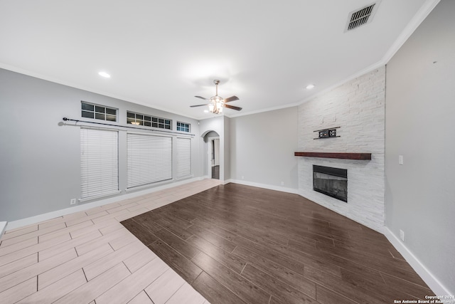 unfurnished living room with ceiling fan, a stone fireplace, light wood-type flooring, and ornamental molding