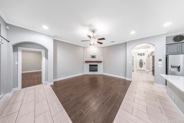 unfurnished living room featuring ceiling fan, a fireplace, crown molding, and stacked washer / dryer