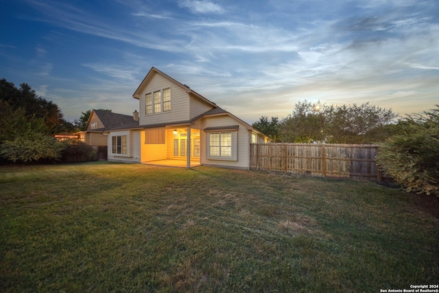 back house at dusk featuring a yard and a patio