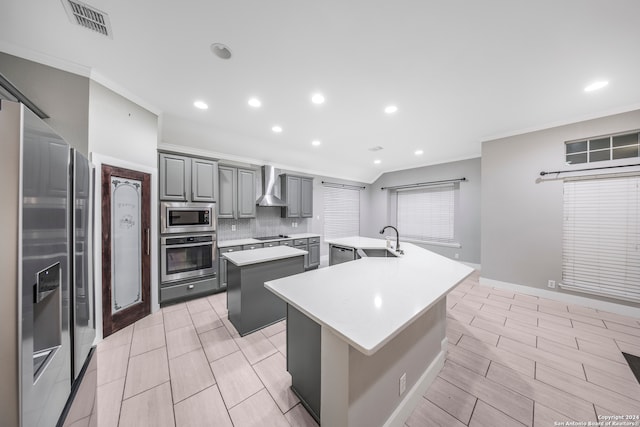 kitchen featuring wall chimney exhaust hood, gray cabinetry, a kitchen island, sink, and stainless steel appliances