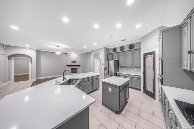 kitchen featuring gray cabinetry, a kitchen island, a large fireplace, sink, and stainless steel appliances