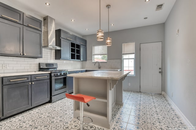 kitchen featuring a breakfast bar, stainless steel range with gas cooktop, hanging light fixtures, a kitchen island, and wall chimney exhaust hood