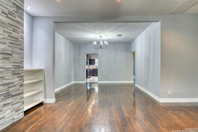 spare room featuring dark wood-type flooring, built in features, and a notable chandelier