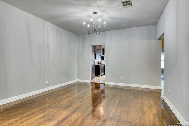 spare room with an inviting chandelier and dark hardwood / wood-style flooring