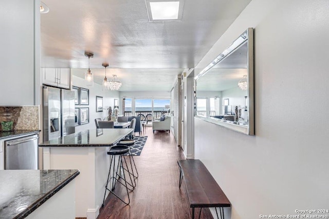 kitchen with white cabinetry, appliances with stainless steel finishes, a breakfast bar, dark stone counters, and dark hardwood / wood-style flooring