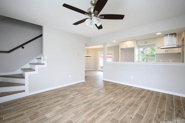 unfurnished living room featuring ceiling fan with notable chandelier, light wood-type flooring, and sink