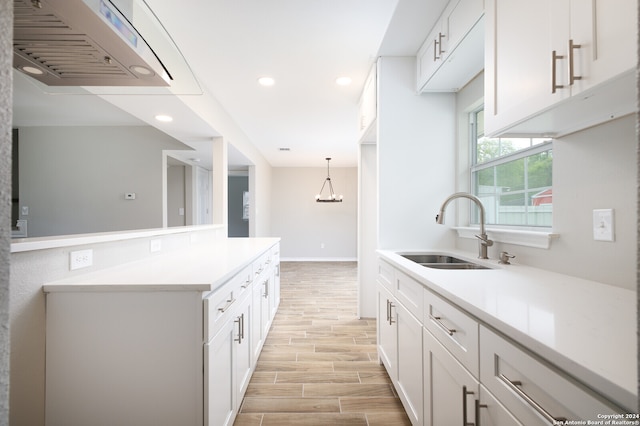 kitchen featuring light wood-type flooring, white cabinets, sink, and decorative light fixtures