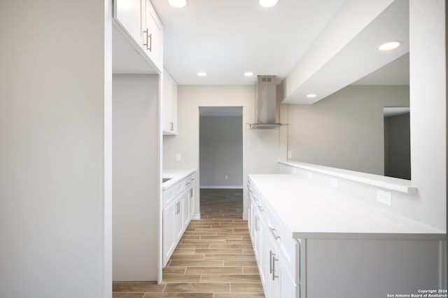 kitchen with light wood-type flooring, wall chimney range hood, and white cabinetry