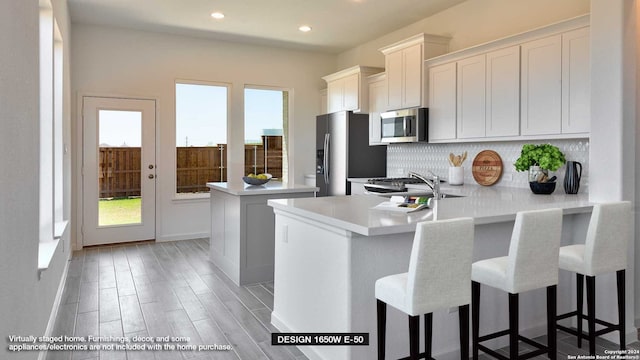 kitchen with tasteful backsplash, white cabinets, kitchen peninsula, stainless steel appliances, and light wood-type flooring