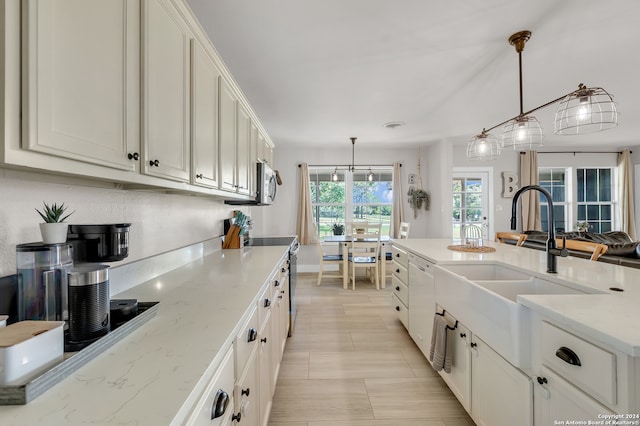 kitchen with appliances with stainless steel finishes, hanging light fixtures, light stone counters, white cabinets, and sink