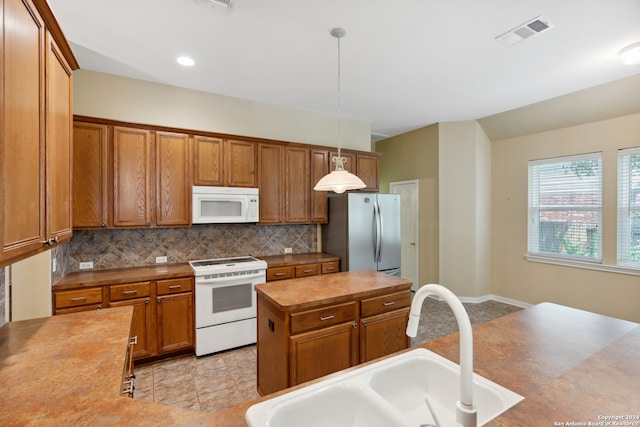 kitchen with pendant lighting, sink, tasteful backsplash, white appliances, and a kitchen island