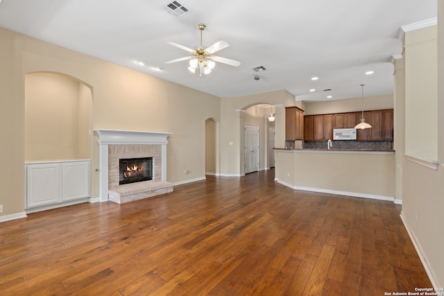 unfurnished living room with dark wood-type flooring, ceiling fan, and a brick fireplace