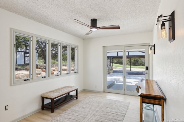 doorway to outside with light wood-type flooring, ceiling fan, and a textured ceiling