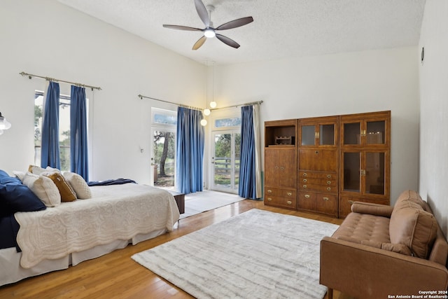 bedroom featuring wood-type flooring, a textured ceiling, access to outside, high vaulted ceiling, and ceiling fan