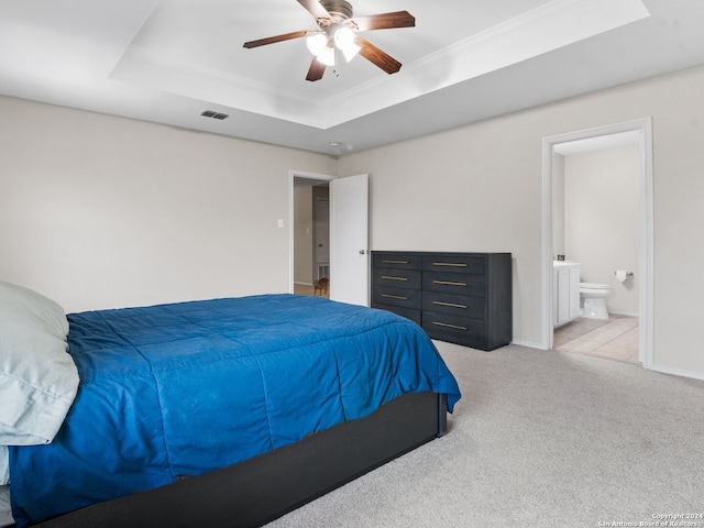 carpeted bedroom with ornamental molding, a tray ceiling, ceiling fan, and ensuite bath