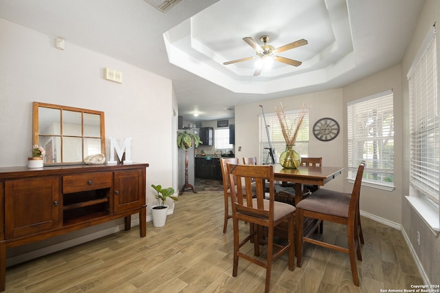 dining area with light hardwood / wood-style floors, a tray ceiling, and ceiling fan