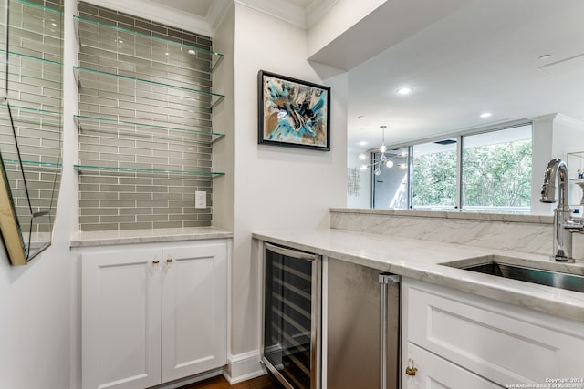 kitchen with wine cooler, light stone counters, sink, white cabinetry, and ornamental molding