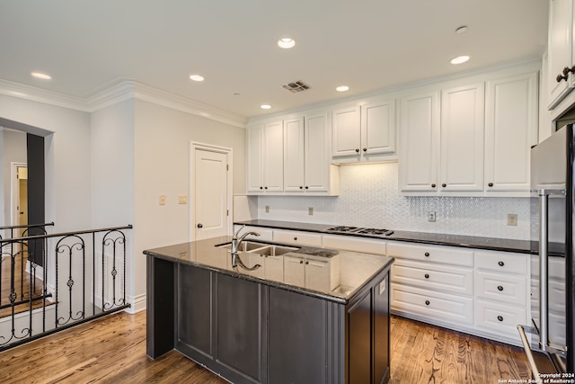 kitchen with dark stone counters, white cabinets, a center island with sink, and light hardwood / wood-style flooring