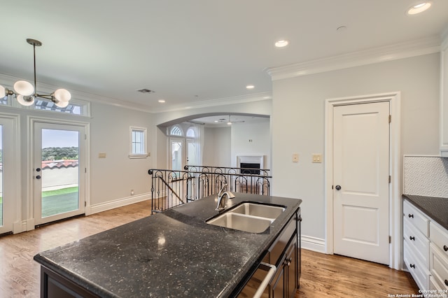 kitchen featuring white cabinets, sink, backsplash, light wood-type flooring, and dark stone countertops